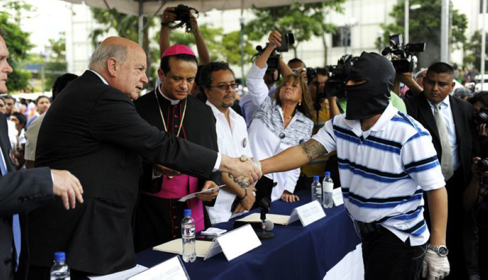 exsecretario de la OEA, saluda a un pandillero enmascarado durante un acto simbólico por la paz en la Plaza Gerardo Barrios, en San Salvador.AFP
