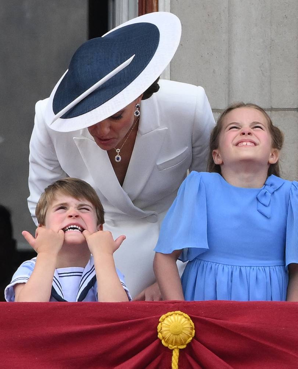 Catherine, duquesa de Cambridge de Gran Bretaña, habla con el Príncipe Louis de Cambridge de Gran Bretaña que está haciendo una mueca, mientras se paran con la Princesa Charlotte de Cambridge de Gran Bretaña para ver un vuelo especial desde el balcón del Palacio de Buckingham después del Desfile del cumpleaños de la Reina.