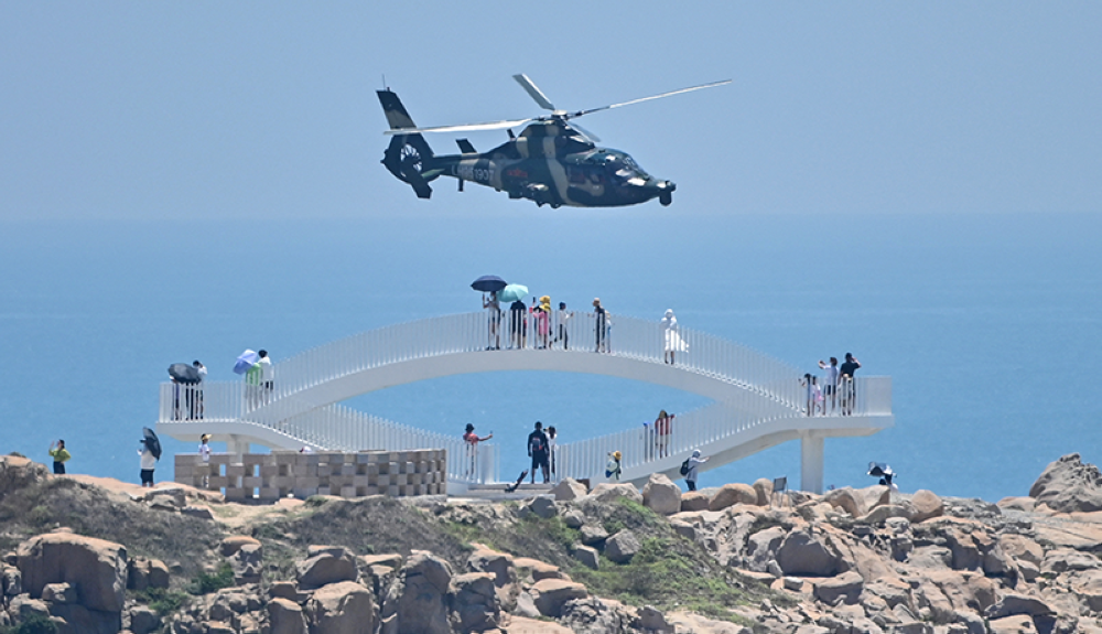 Los turistas observan cómo un helicóptero militar chino sobrevuela la isla de Pingtan como parte de ejercicios militares en el estrecho de Taiwán.AFP