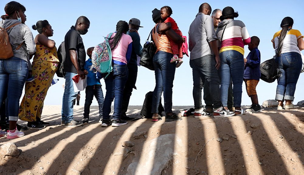 Inmigrantes de Haití, que cruzaron a través de una brecha en la barrera fronteriza entre Estados Unidos y México, esperan en fila para ser procesados ​​por la Patrulla Fronteriza en Arizona.AFP