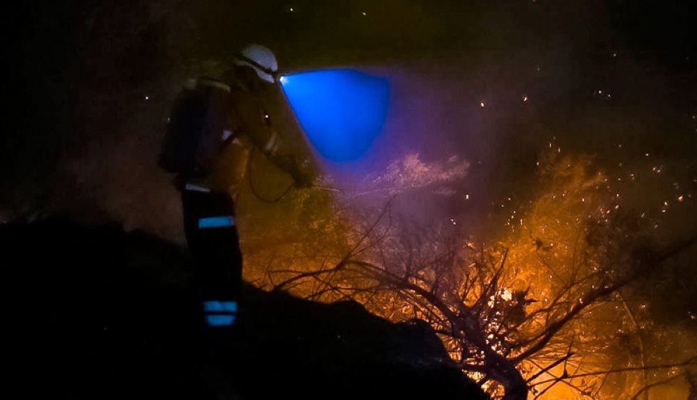 Bombero ilumina una barranca donde se concentra el fuego en la faldas del volcán de San Salvador. Cortesía SDP