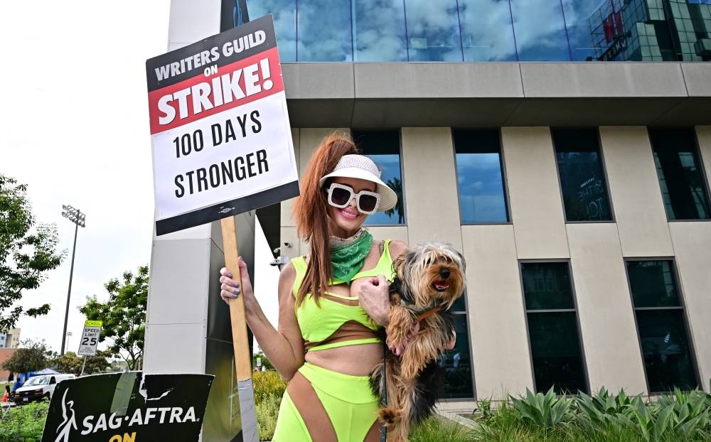 La actriz Phoebe Price también se fue con todo y su perro a apoyar las protestas de los sindicatos de actores y guionistas que exigen mejoras salariales afuera de Netflix, en Hollywood, California. / Foto: AFP