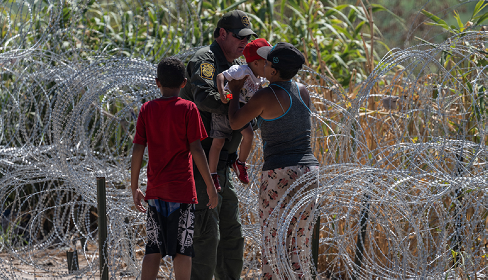 Un miembro de la Patrulla Fronteriza y de Aduanas de EE. UU. entrega un niño a una mujer mientras los migrantes cruzan el Río Grande.AFP