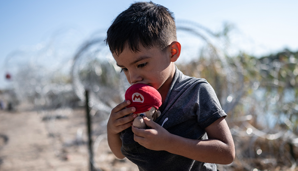 Un niño migrante de El Salvador besa un muñeco Mario antes de caminar hacia un área de procesamiento con su familia.AFP