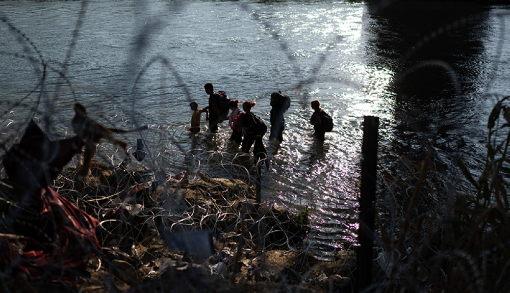 Migrantes caminan por el río Grande mientras buscan una rotura en el alambre de púas en la frontera entre Estados Unidos y México en Eagle Pass, Texas.AFP