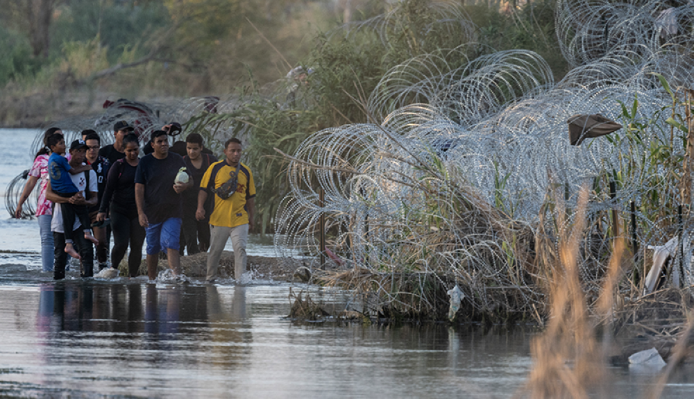 Migrantes caminan a lo largo de alambre de púas en busca de un lugar para cruzar en el río Grande en la frontera entre Estados Unidos y México en Eagle Pass, Texas.AFP