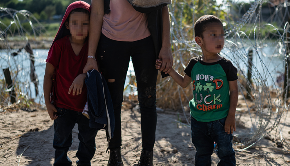 Niños de El Salvador toman la mano de su madre antes de caminar hacia un área de procesamiento después de cruzar el río Grande en la frontera entre Estados Unidos y México en Eagle Pass.AFP