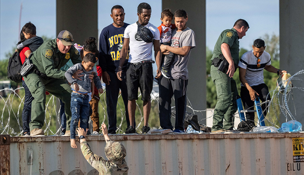 Agentes fronterizos ayudan a los migrantes a cruzas a sus hijos en un áreas con puas.AFP