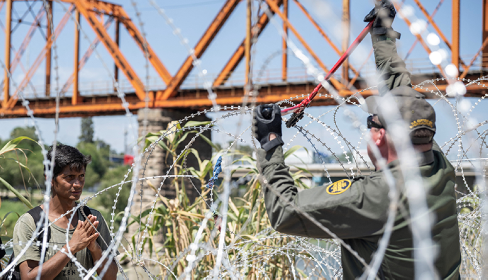 Un agente fronterizo corta alambre con púas para dejar pasar a un migrante en sur de Texas a orillas del rió Grande.AFP