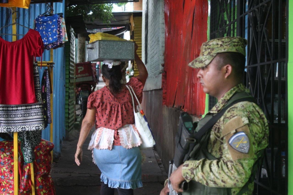 Un soldado de la Fuerza Armada a un costado mientras pasa un peatón en la zona de Valle Verde, Apopa. / Emerson del Cid.