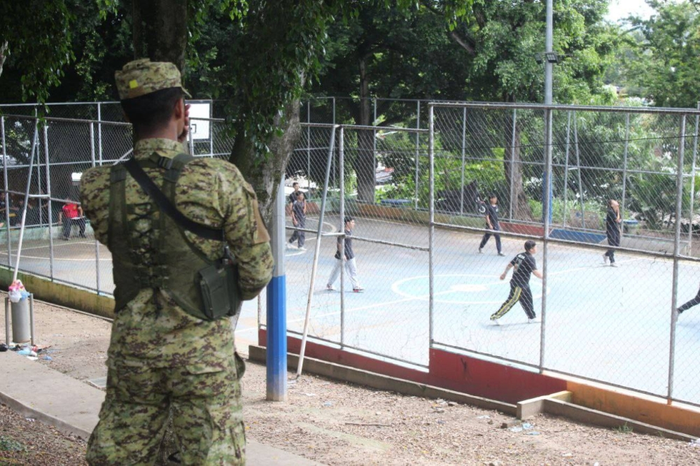 Un soldado vigila una cancha en Apopa mientras los niños juegan en el cerco militar implementado en Valle Verde, Apopa / Emerson del Cid.