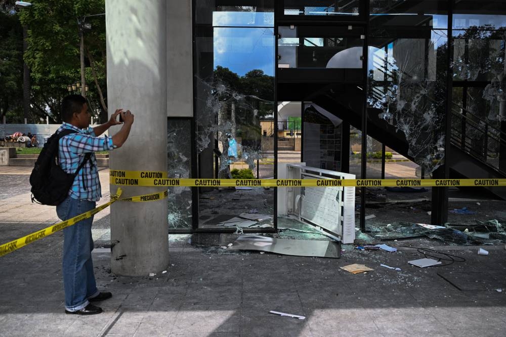 Una persona se acerca a hacer fotos en uno de los lugares donde manifestantes destruyeron ciertas propiedades, por exigir la renuncia de la fiscal general, Consuelo Porras y del fiscal Curruchiche. / AFP