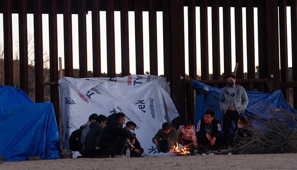 Los nuevos migrantes intentan mantenerse calientes junto a un incendio instalado a lo largo del muro fronterizo que separa México y Estados Unidos en Jacumba, California.AFP