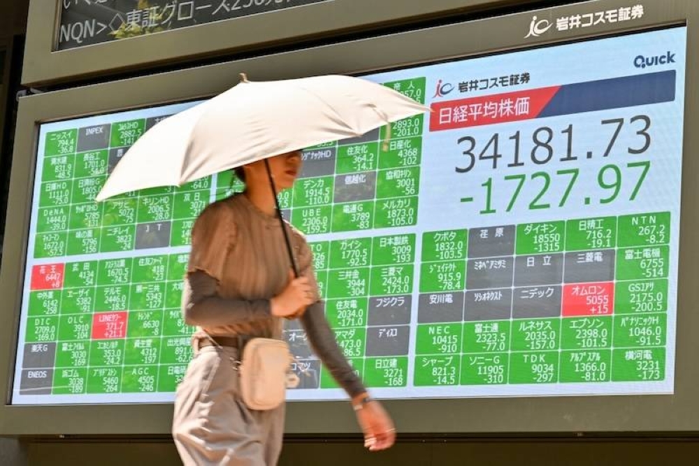 Un transeúnte pasa frente a un cartel en el Tokyo Stock Exchange, que ilustra la caída del índice bursátil japonés./AFP,image_description: