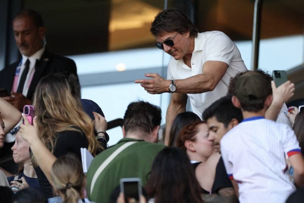 El actor estadounidense Tom Cruise firma autógrafos mientras asiste al partido de fútbol final por la medalla de oro femenina entre Brasil y Estados Unidos durante los Juegos. / AFP.,image_description: