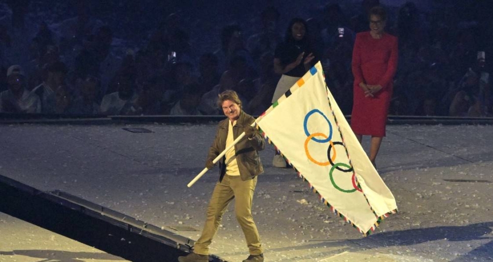 El actor estadounidense Tom Cruise recibe la bandera olímpica de manos de la gimnasta estadounidense Simone Biles y de la alcaldesa de Los Ángeles, Karen Bass, durante la ceremonia de clausura de los Juegos Olímpicos de París 2024 en el Stade de France, en SaintDenis, en las afueras de París. / AFP.,image_description: