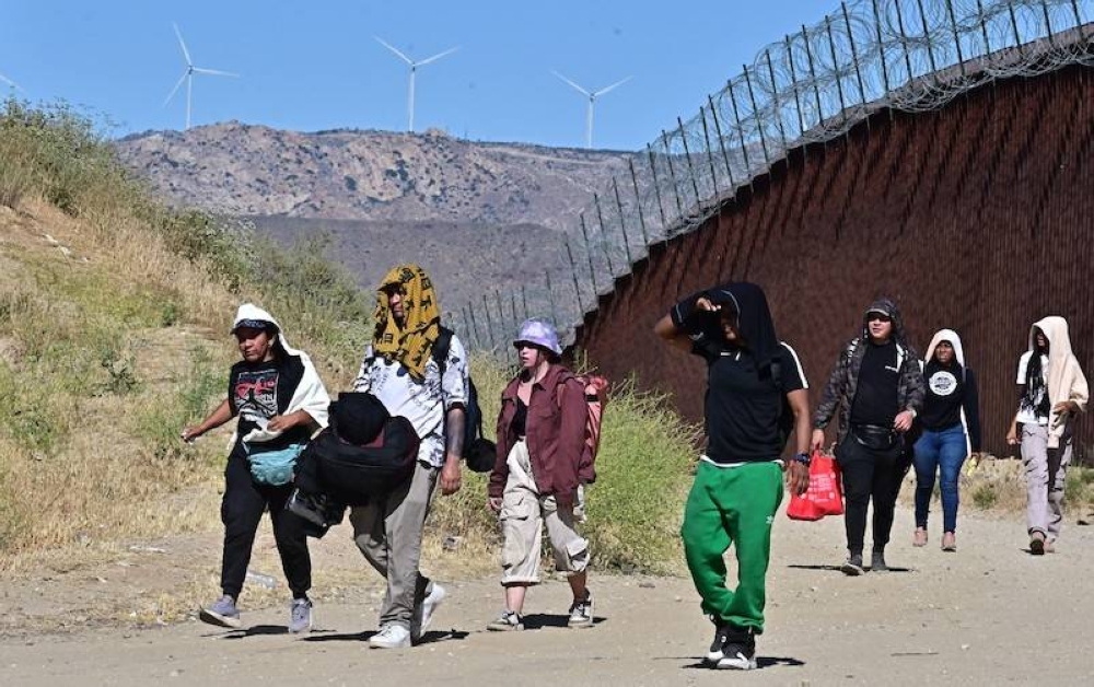 Migrantes caminan por el lado estadounidense del muro fronterizo en Jacumba Hot Springs, California, el 5 de junio. / AFP.,image_description: