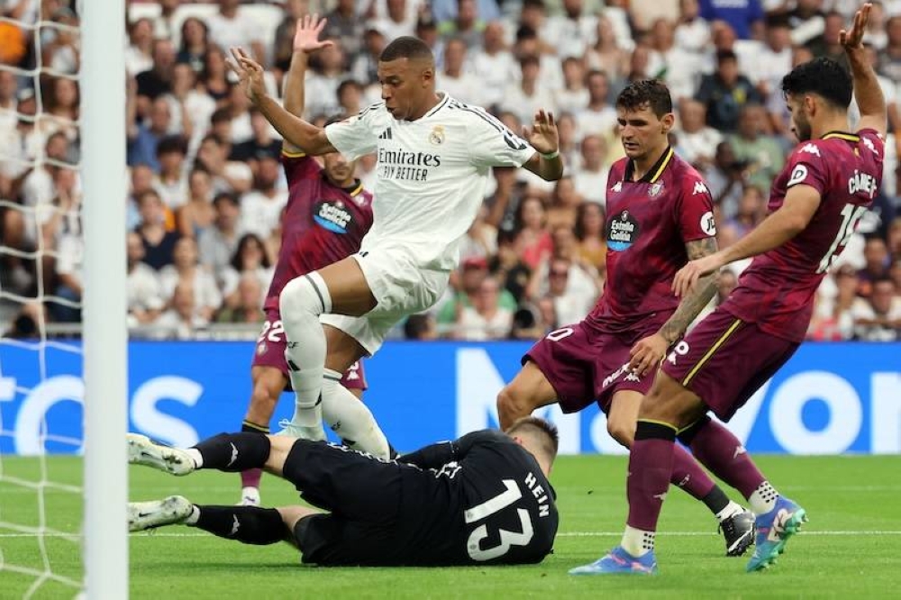 El delantero francés del Real Madrid, Kylian Mbappé izq., y el portero estonio del Real Valladolid, Karl Jakob Hein, disputan el balón durante el partido de fútbol de la liga española entre el Real Madrid CF y el Real Valladolid FC en el estadio Santiago Bernabéu de Madrid el 25 de agosto./ AFP,image_description: