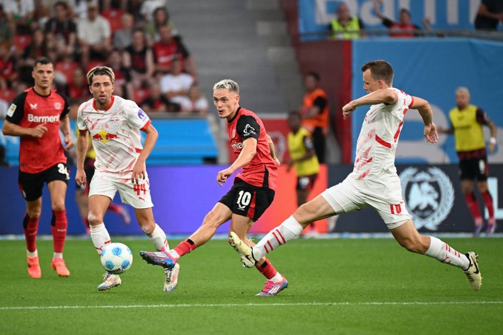 Florian Wirtz, del Leverkusen, reamta ante la marca de Lukas Klostermann. / AFP,image_description: