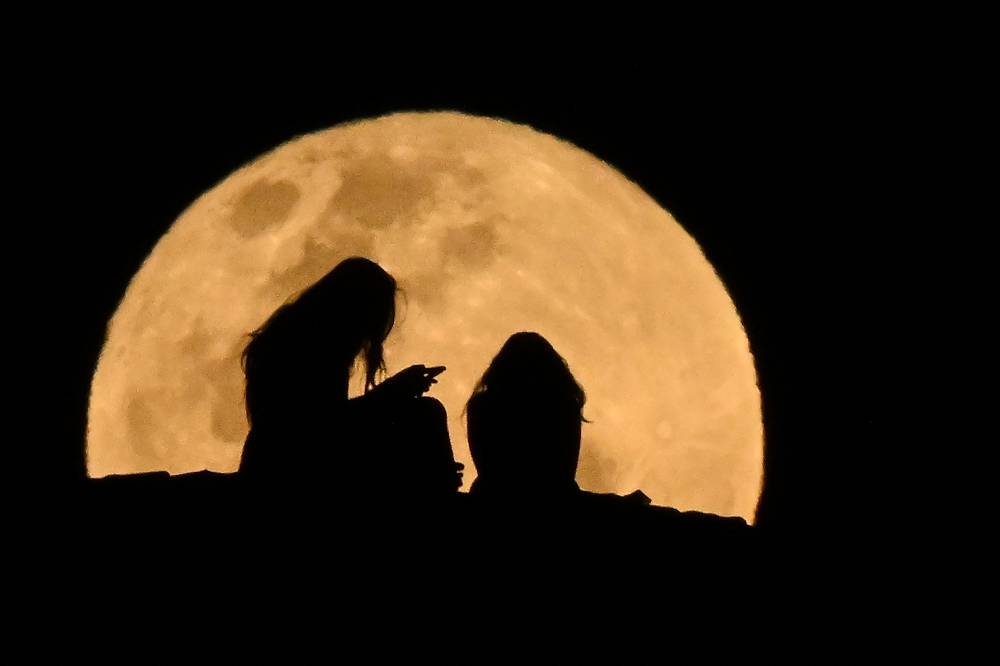 Chicas de Queenscliff observan la luna llena que sale en la playa de Manly, en Sídney, el 18 de septiembre de 2024. (Foto de Saeed KHAN / AFP)