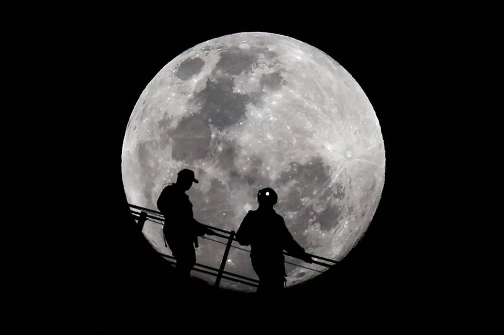 La sombra de dos escaladores  contra la luna llena mientras descienden de la cima del puente del puerto de Sídney, Australia, el 17 de septiembre de 2024. Foto de Saeed KHAN / AFP,image_description: