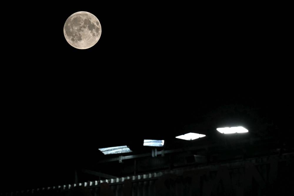 Una luna llena, también llamada Luna de la Cosecha, y una de las 4 superlunas de este año, se ve elevándose sobre las luces de Old Trafford en Manchester, noroeste de Inglaterra, el 17 de septiembre de 2024, durante el partido de fútbol de tercera ronda de la Copa de la Liga inglesa entre Manchester United y Barnsley. Foto de Paul ELLIS / AFP