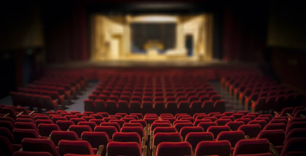 Si deseas asistir a su ponencia, debes acudir a la Alianza Francesa en Calle y Colonia la Mascota, pasaje Nu00b0 2 y casa Nu00b0 547, San Salvador.,image_description:Empty red armchairs of a theater ready for a show