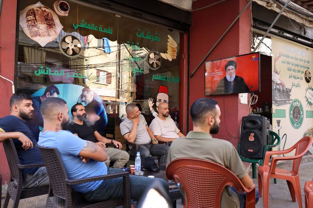 La gente observa en una pantalla de televisión al líder de Hezbolá, Hassan Nasrallah, mientras se dirige a la nación a través de un enlace de video, en un café en el barrio de Shiyah, en los suburbios del sur de Beirut, el 19 de septiembre de 2024. Foto de ANWAR AMRO / AFP,image_description: