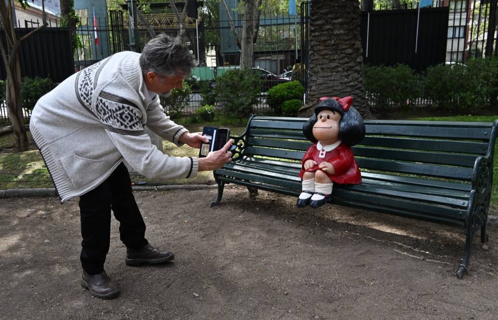 El escultor argentino Pablo Irrgang toma una fotografía de su escultura del personaje de historieta Mafalda luego de su inauguración por parte de las autoridades locales en Santiago el 27 de septiembre de 2024. Foto de RODRIGO ARANGUA / AFP,image_description: