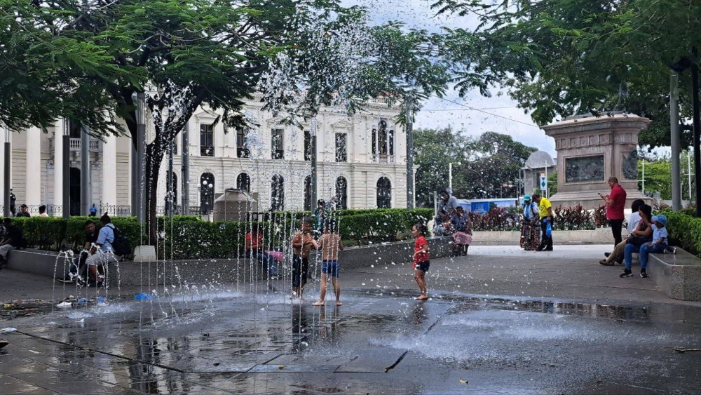 Tres niños juegan y se refrescan en la fuente de la plaza Gerardo Barrios en el Centro Histórico de San Salvador. / Iliana Cornejo.,image_description: