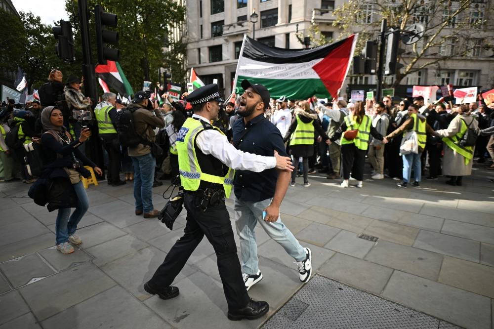 Un oficial de policía frena a un activista pro palestino que intenta acercarse a los contramanifestantes pro israelíes durante una marcha en Londres. /AFP