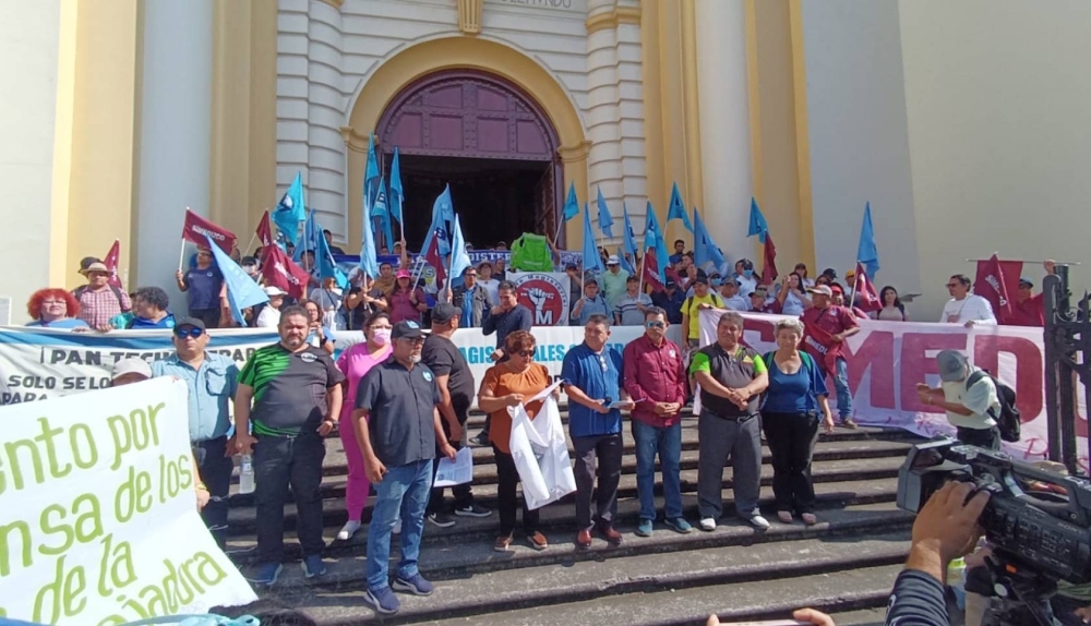 Diferentes sindicatos del sistema de salud y educación se reunieron este día frente a la Catedral Metropolitana de San Salvador para anunciar una jornada de u201cluchau201d por el congelamiento de escalafones. /Bases Magisterialesn,image_description: