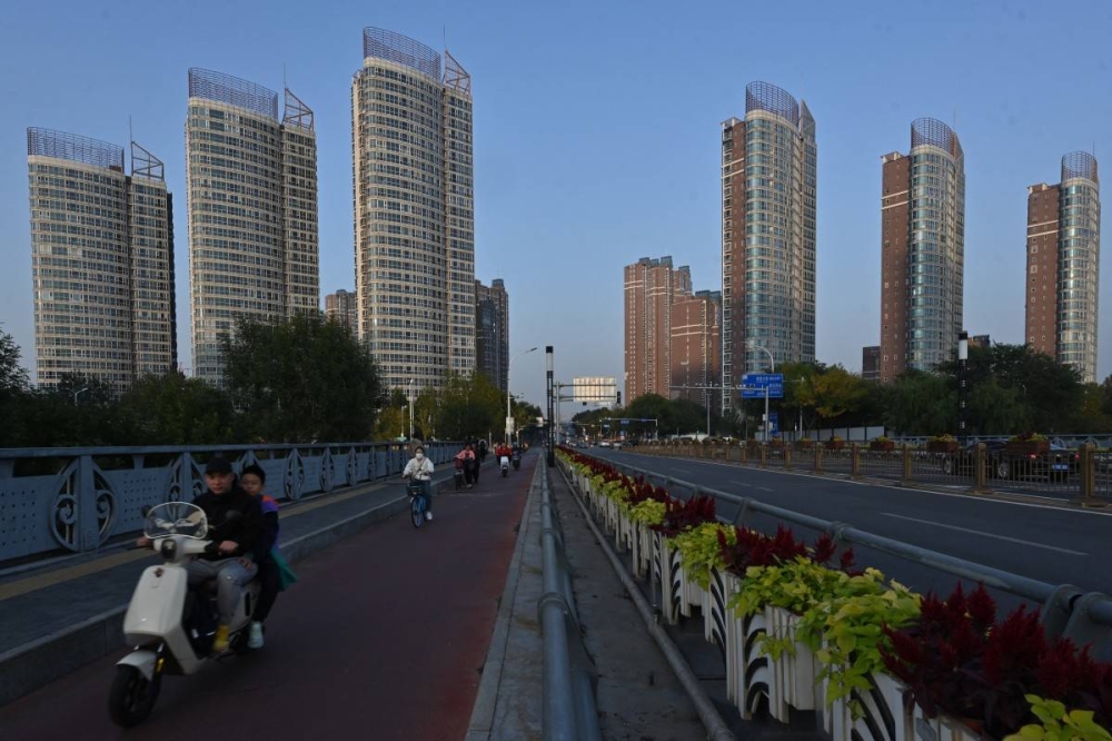 La gente viaja mientras se ven edificios de gran altura al fondo en Beijing el 11 de octubre de 2024. / AFP.,image_description: