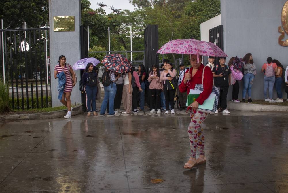 Un grupo de personas, entre ellos estudiantes universitarios, se resguardan de la lluvia en San Salvador. / Lisbeth Ayala.,image_description: