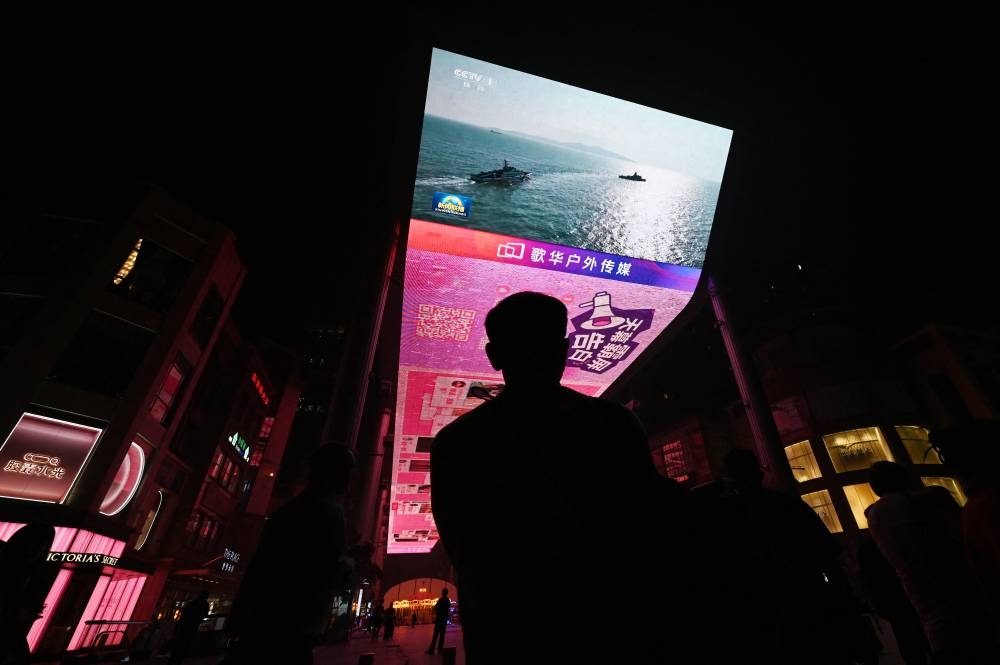 Un hombre mira un programa de noticias sobre ejercicios militares chinos en Taiwán, en una pantalla gigante afuera de un centro comercial en Beijing el 14 de octubre de 2024. GREG BAKER/AFP,image_description: