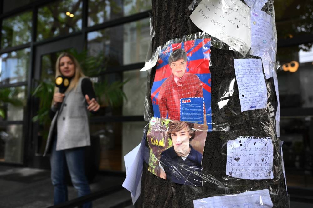 Un periodista señala cartas escritas por fans en honor al cantante británico Liam Payne frente al hotel donde murió en Buenos Aires el 17 de octubre de 2024. Luis ROBAYO / AFP,image_description: