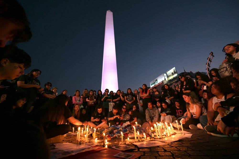 Los fanáticos encienden velas mientras rinden homenaje al fallecido cantante británico Liam Payne en el Obelisco de Buenos Aires el 17 de octubre de 2024. Los tributos se derramaron por el cantante británico Liam Payne, ex miembro de la exitosa banda de chicos One Direction, luego de que se lanzara hasta la muerte desde el balcón de un hotel de Buenos Aires el 16 de octubre. Foto de JUAN MABROMATA / AFP,image_description: