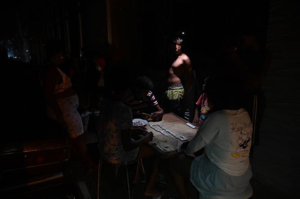 Un grupo de cubanos juegan al dominó en la oscuridad en una calle durante un apagón nacional causado por un fallo en la red eléctrica en La Habana. /AFP,image_description: