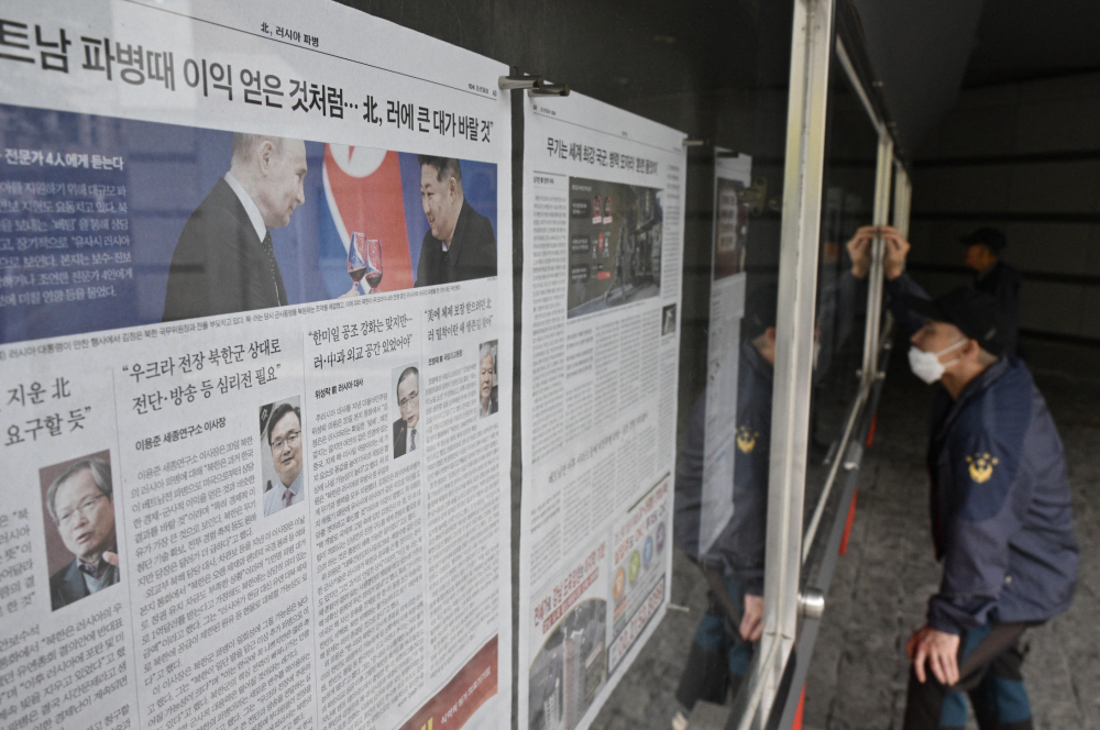 Un hombre lee un periódico expuesto al público en una calle de Seúl el 21 de octubre de 2024, que muestra una foto izq. del líder norcoreano Kim Jong Un der. y el presidente ruso Vladimir Putin brindando en un banquete en Pyongyang a principios de este año. Anthony Wallace/ AFP,image_description: