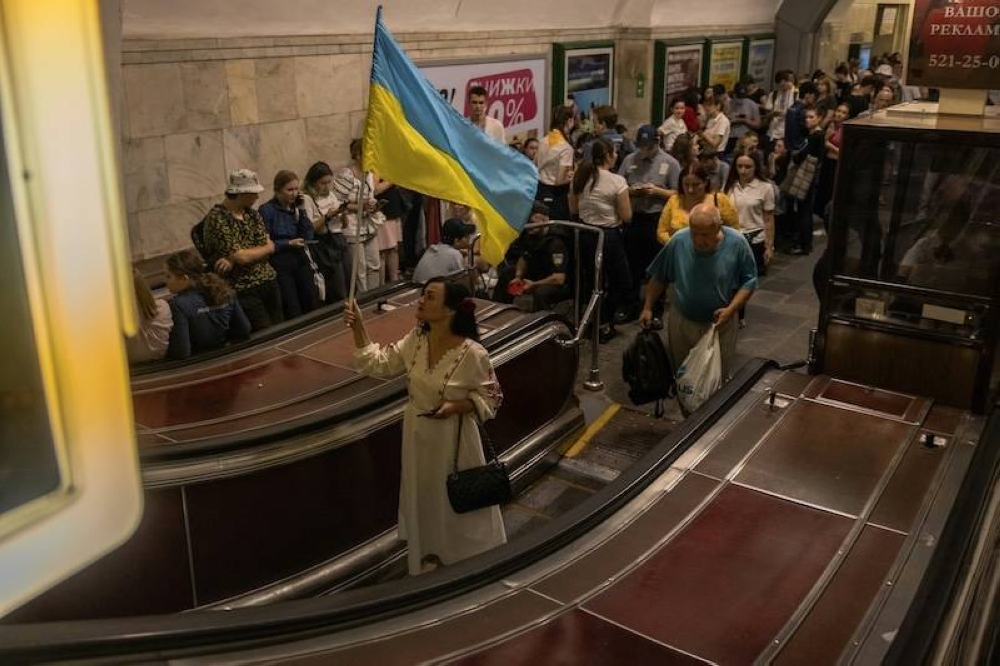 Una mujer ondea una bandera nacional ucraniana mientras la gente se refugia en la estación de metro Khreshchatyk en la capital de ese país, durante una alarma de ataque aéreo ruso. /AFP,image_description: