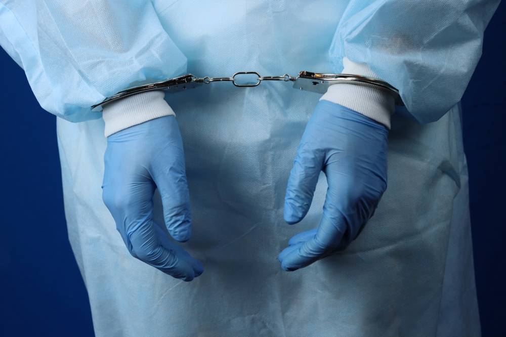 La enfermera estaría en la delegación de Zacamil, según los sindicatos. ,image_description:Doctor handcuffed, hands closeup, concept of medical corruption, bribery, crime