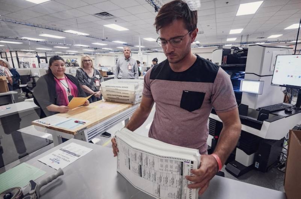 Un trabajador electoral procesa una pila de papeletas de las elecciones generales de 2024 con la máquina de tabulación frente a observadores de diferentes partidos en el Centro de Tabulación y Elecciones del Condado de Maricopa MCTEC en Phoenix, Arizona./AFP,image_description: