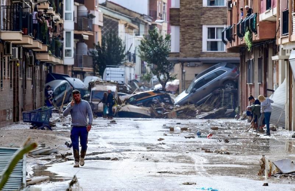 Residentes de Picanya, cerca de Valencia, en el este de España, caminan frente a automóviles apilados en una calle cubierta de barro luego de las inundaciones./ AFP,image_description: