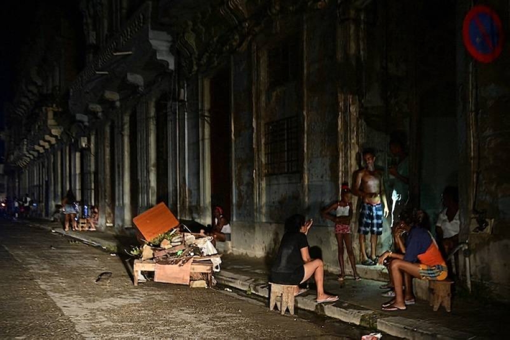 Un grupo de cubanos conversan de noche en una calle durante un apagón nacional causado por una falla en la red en La Habana el 18 de octubre de 2024./AFP.,image_description: