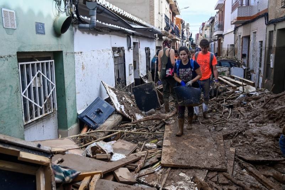 Los voluntarios que llegaron para ayudar a limpiar los escombros avanzan por una calle llena de vehículos y escombros el 2 de noviembre de 2024, tras las devastadoras inundaciones en la ciudad de Paiporta, en la región de Valencia, este de España. /AFP,image_description: