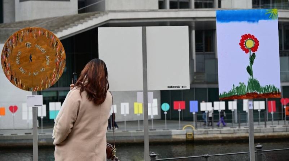 Una mujer toma una fotografía en el río Spree marca el antiguo curso del muro antes de las celebraciones del 35u00ba aniversario de la caída del Muro de Berlín. / AFP.,image_description: