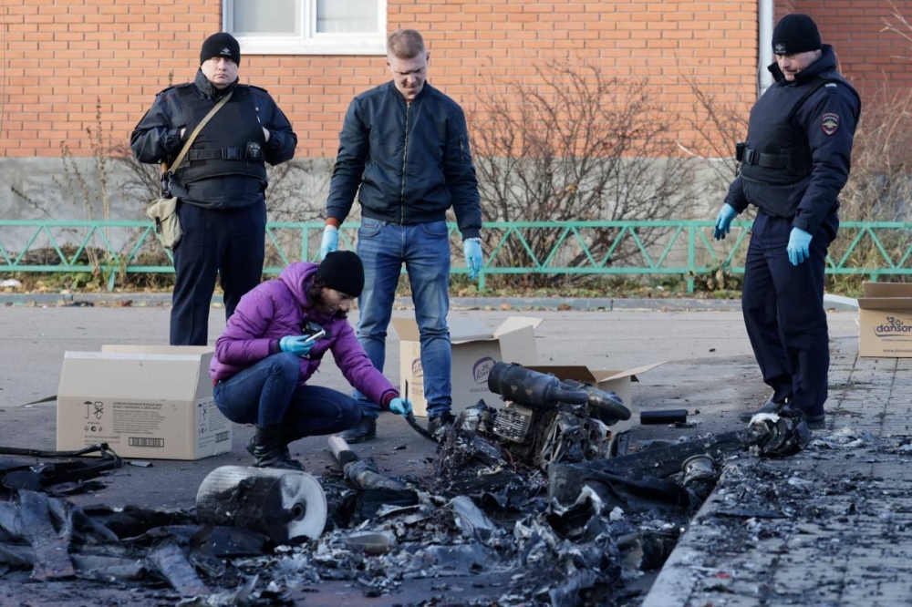 Agentes policiales rusos inspeccionan los restos de un dron tras un ataque con dron en la aldea de Sofyino, región de Moscú, el 10 de noviembre de 2024. / AFP.,image_description: