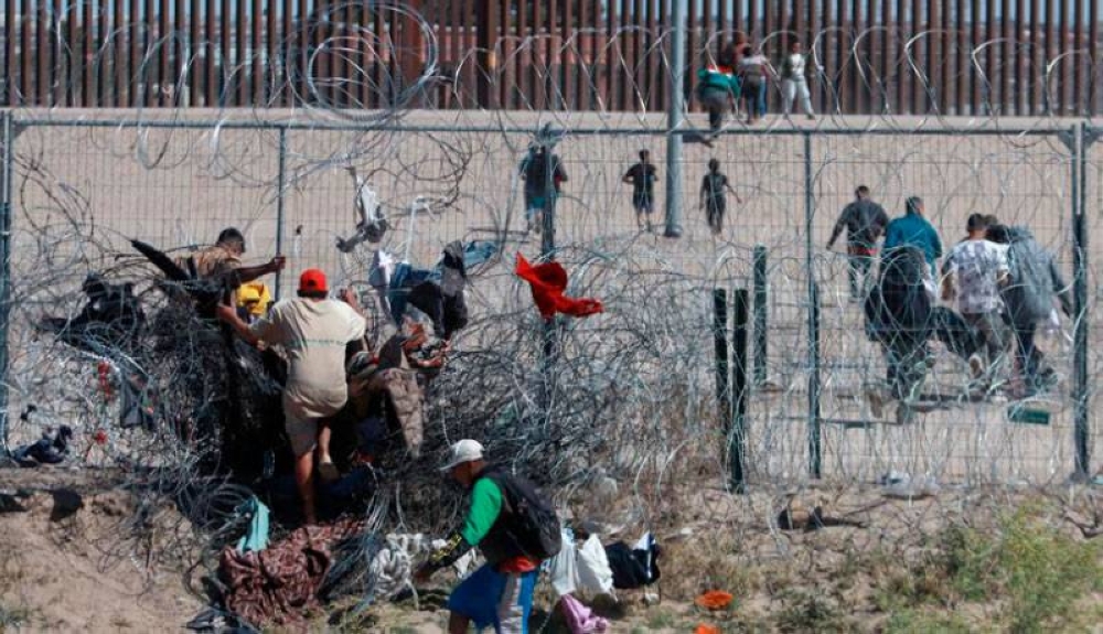 Migrantes cruzan una alambrada de navajas y púas, en la frontera que divide a México de los Estados Unidos en Ciudad Juárez México.,image_description: