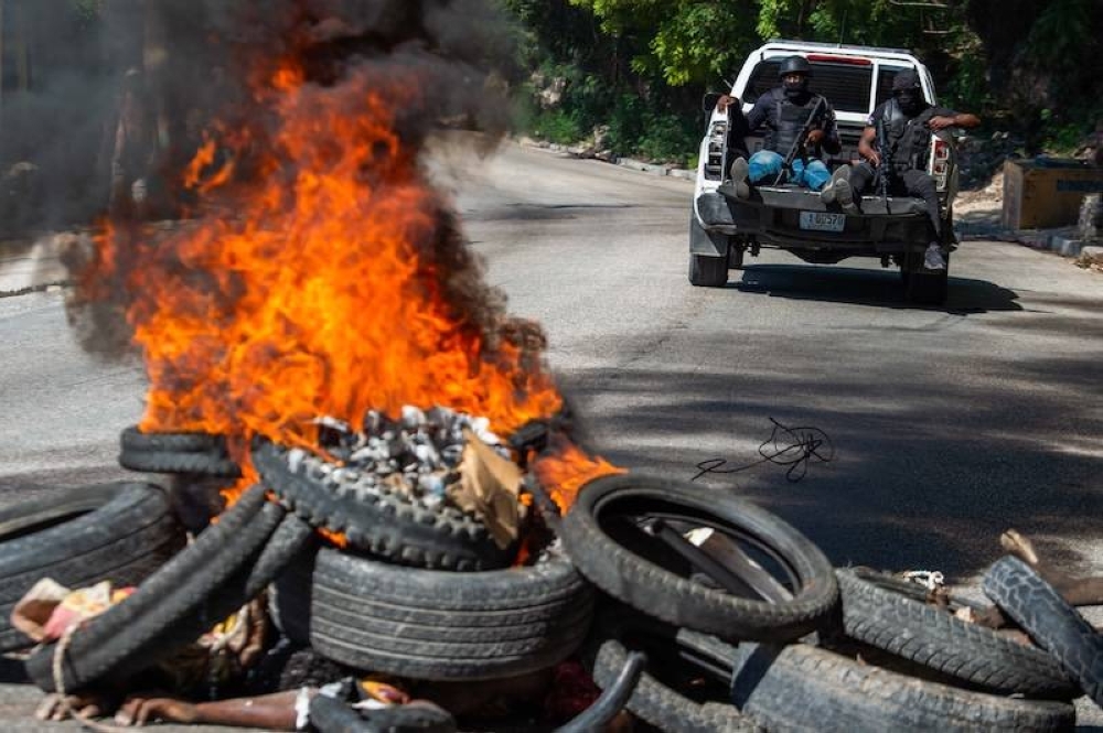 Miembros de la Policía Nacional de Haití patrullan mientras se queman cuerpos de presuntos pandilleros en primer plano en PetionVille, un suburbio de Puerto Príncipe, Haití. La policía y grupos civiles de autodefensa mataron a 28 presuntos pandilleros en la capital haitiana, Puerto Príncipe, en una operación nocturna, mientras el gobierno busca recuperar parte del control de la ciudad./AFP,image_description: