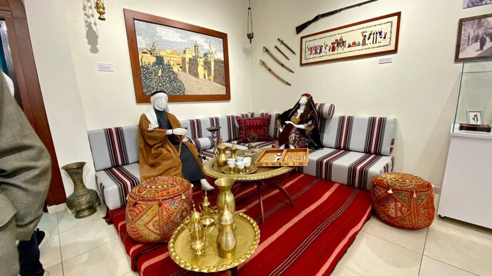 Modelo de una sala árabe-palestina, que incluye una alfombra beduina, la representación de un patriarca y una mujer palestina; un juego de mesa tallado en madera llamado “Shesh Besh” y utensilios en cobre como jarrones y café.